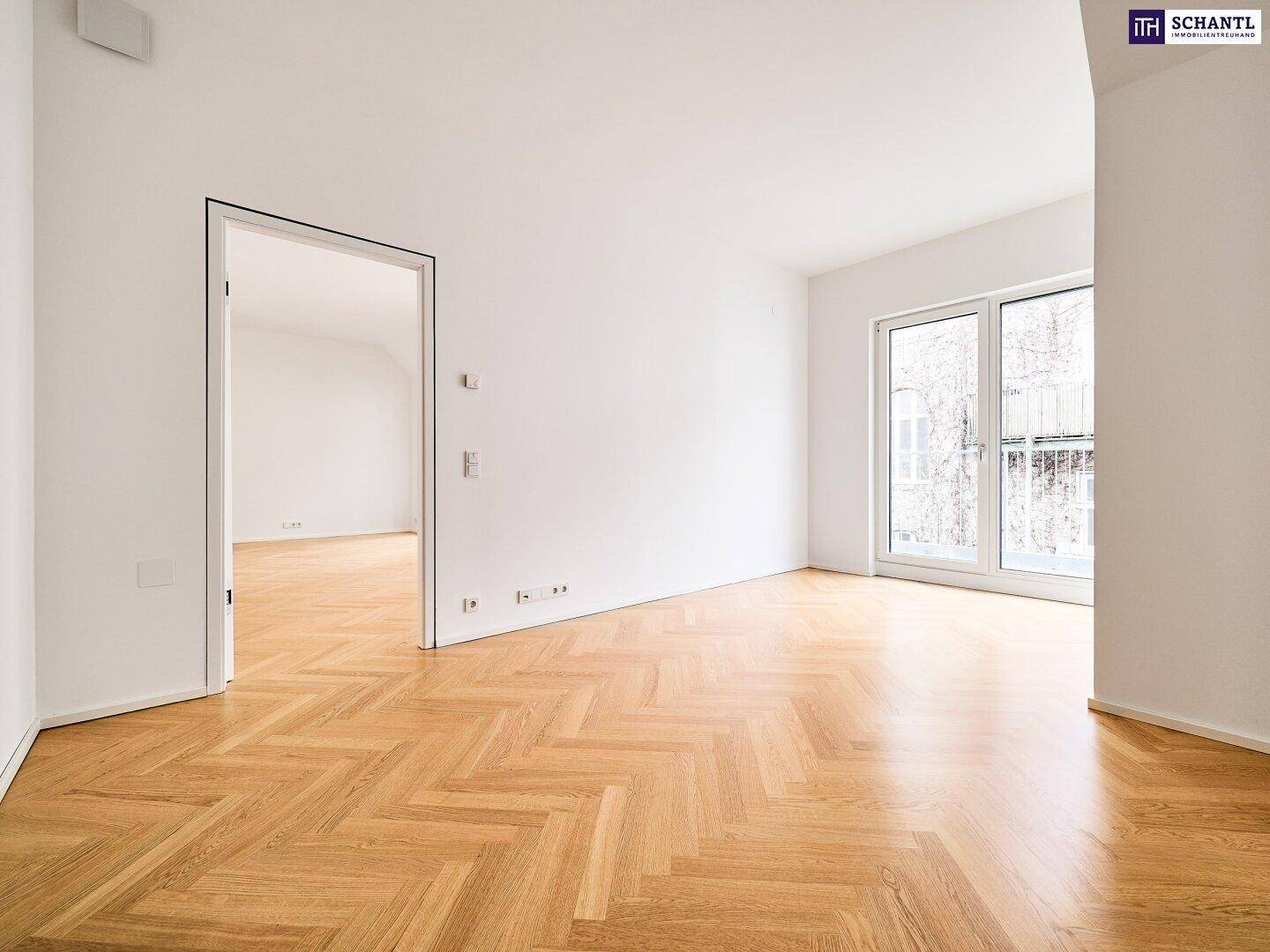 Heller, leerer Raum mit Fischgrätparkett und Zugang zu einem französischen Balkon.