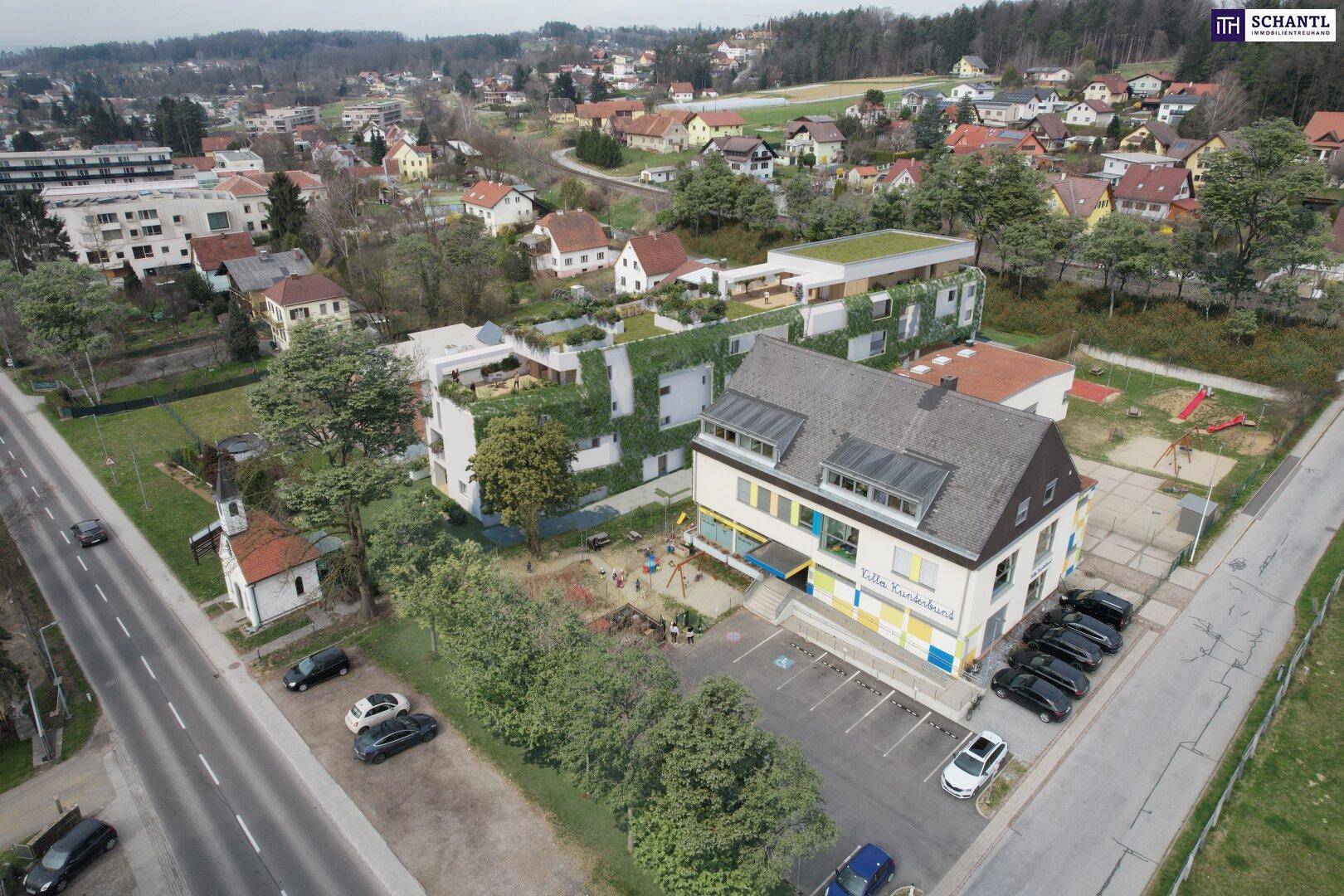 Vogelperspektive eines modernen Wohngebäudes mit begrünten Fassaden, umgeben von Wohnbebauung und einem Kindergarten.
