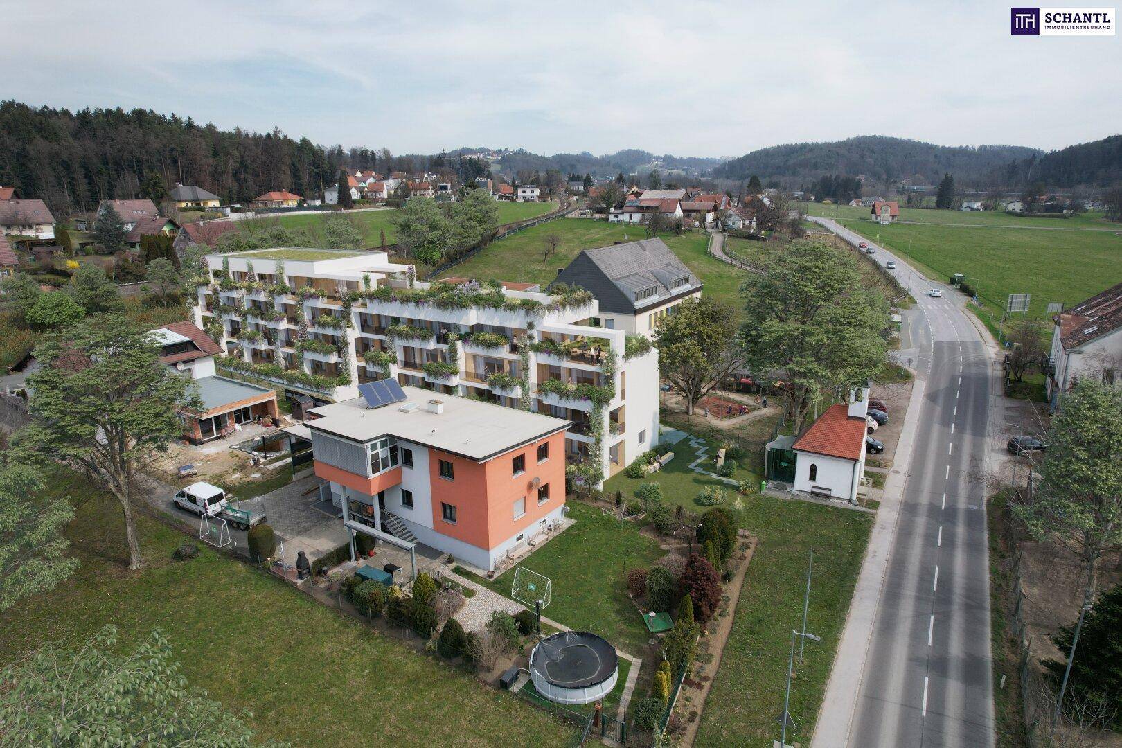 Weitläufige Luftaufnahme eines modernen Wohnkomplexes mit begrünten Balkonen und Dächern in ländlicher Umgebung.