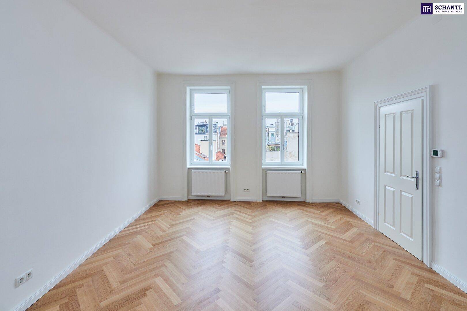 Helles Zimmer mit Fischgrätparkettboden, weißen Wänden und zwei großen Fenstern.