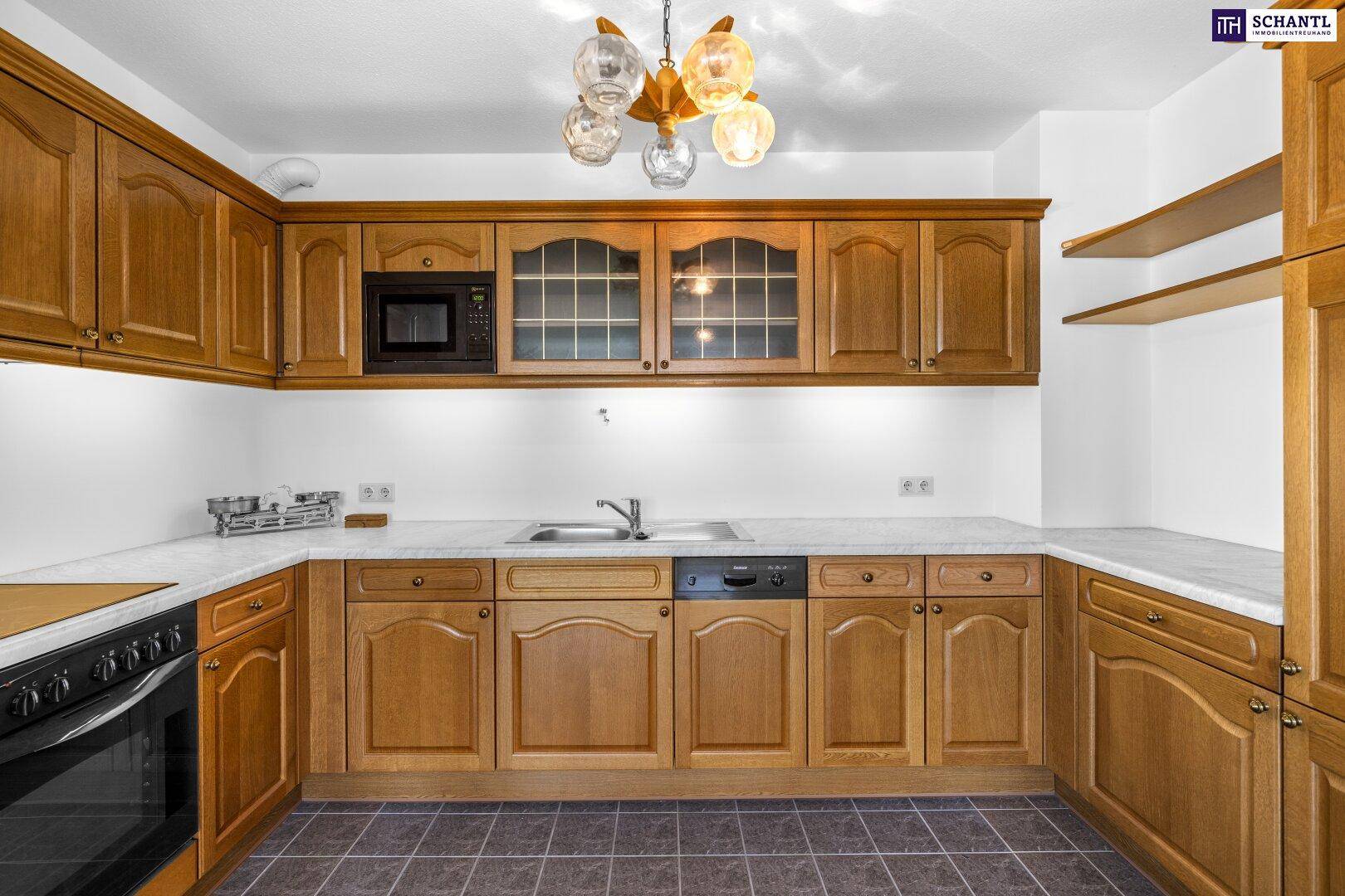 Küche mit Holzschränken, Einbaugeräten und traditioneller Deckenleuchte, bereit zur Modernisierung.