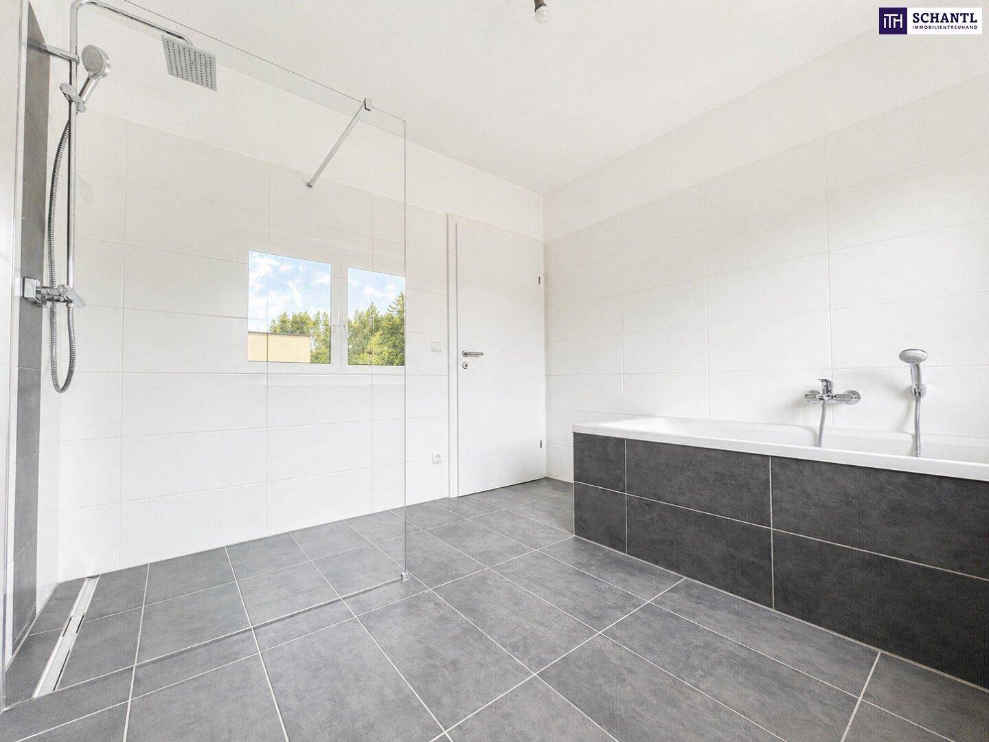 Modernes Badezimmer mit grauen Bodenfliesen, ebenerdiger Dusche und Badewanne mit dunkler Verkleidung.
