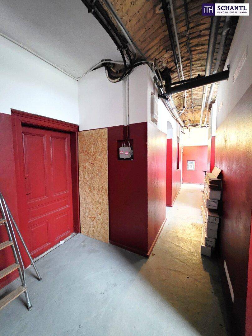 Kellerflur mit roten Wänden, sichtbaren Rohren an der Decke und einer Leiter.