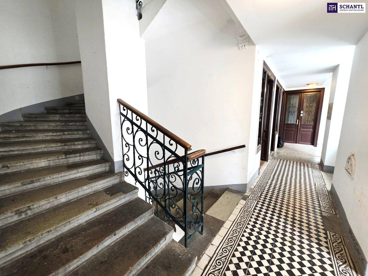 Historisches Treppenhaus mit schmiedeeisernem Geländer und Schachbrettmuster-Fliesenboden.