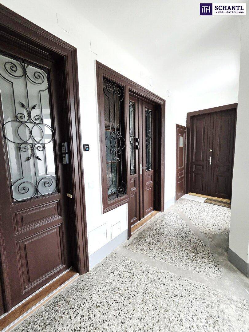 Langer Flur mit dunklen Holztüren und Terrazzoboden in einem Altbau.