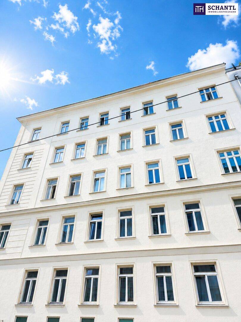 Helle Fassade eines Wohngebäudes mit vielen Fenstern unter strahlend blauem Himmel.