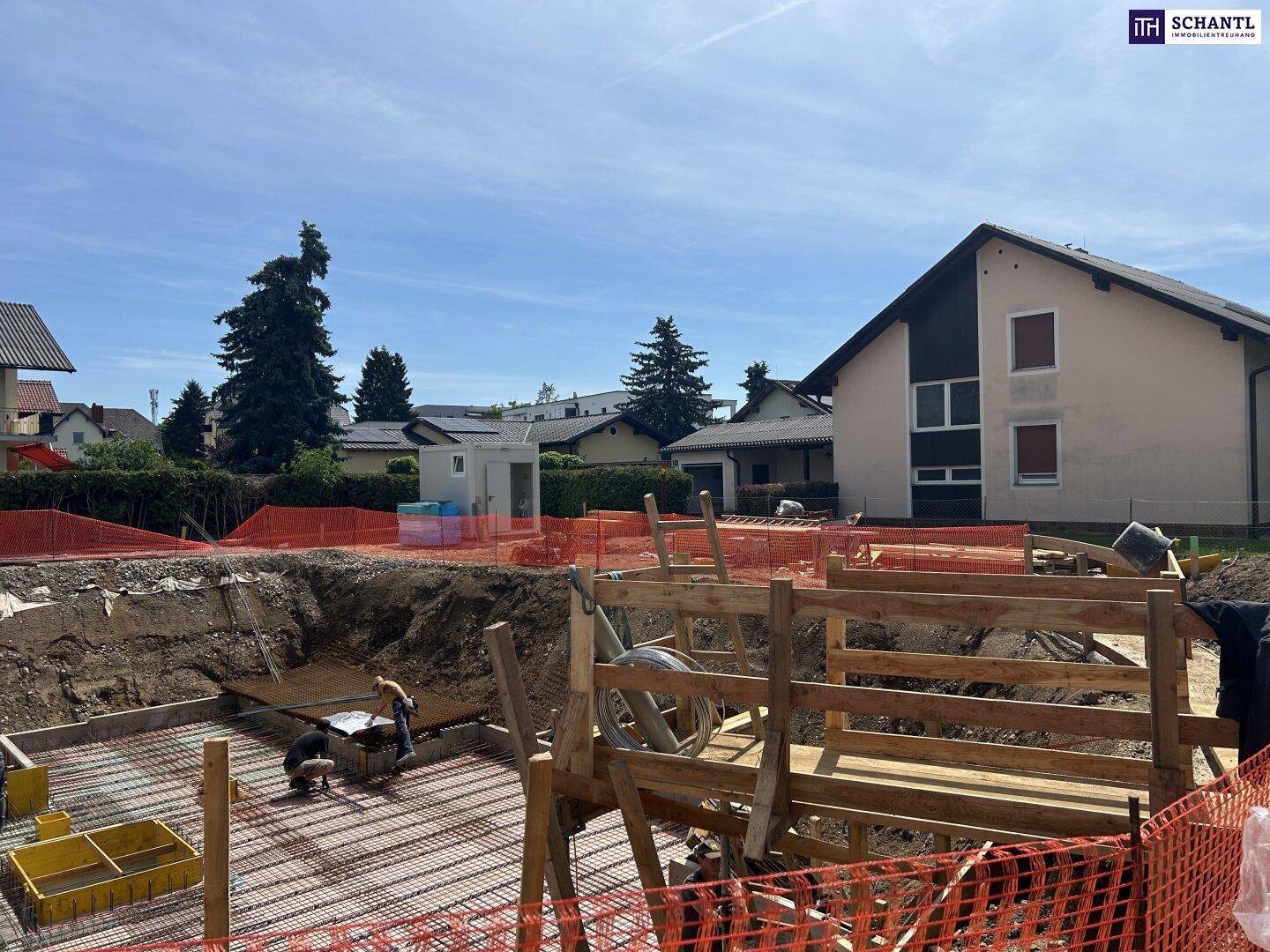 Bauarbeiten am Fundament mit sichtbarer Bewehrung und angrenzenden Häusern in einer ländlichen Umgebung.