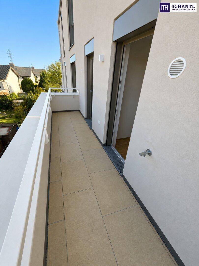 Heller Balkon mit Fliesenboden und Zugang zu einem Innenraum, umgeben von Wohngebäuden.