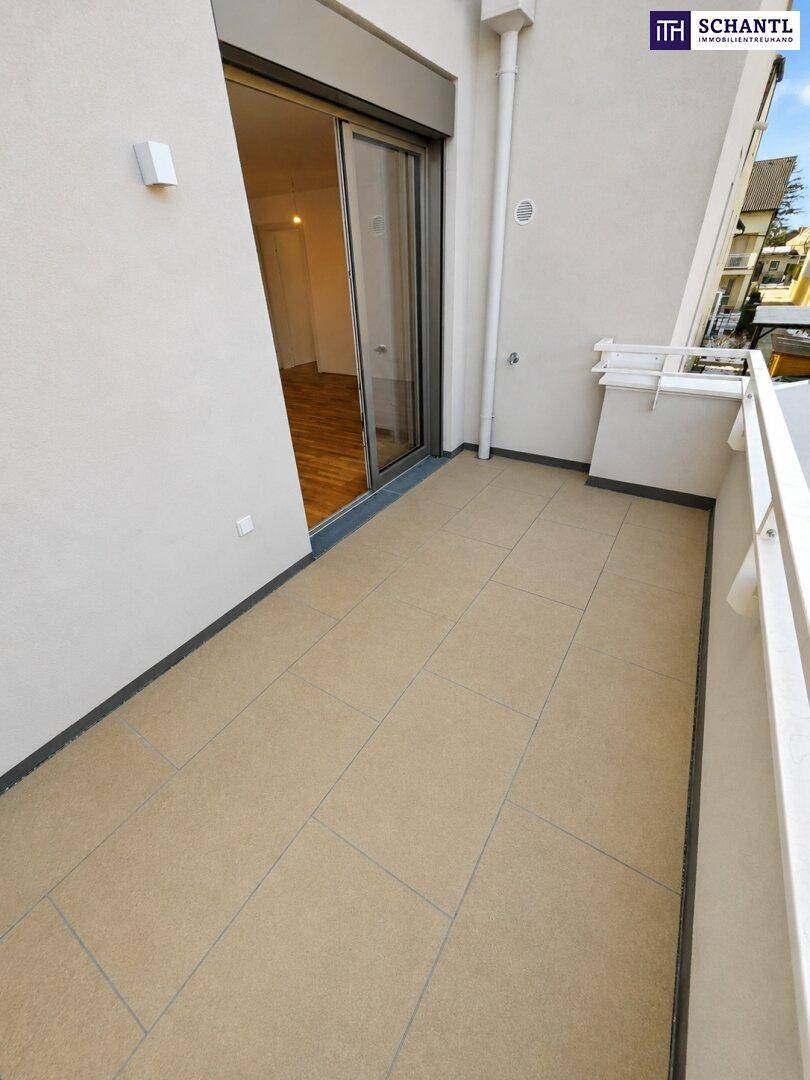 Heller Balkon mit beigefarbenen Fliesen und Zugang zu einem Innenraum mit Parkettboden.