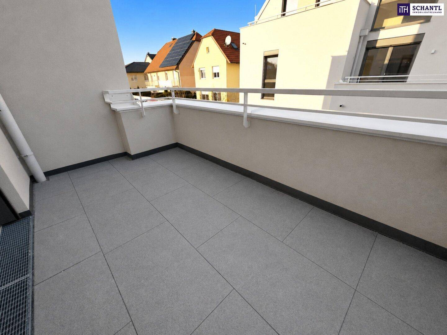 Geräumiger Balkon mit grauen Fliesen und weißem Geländer, bietet Blick auf die umliegenden Häuser.