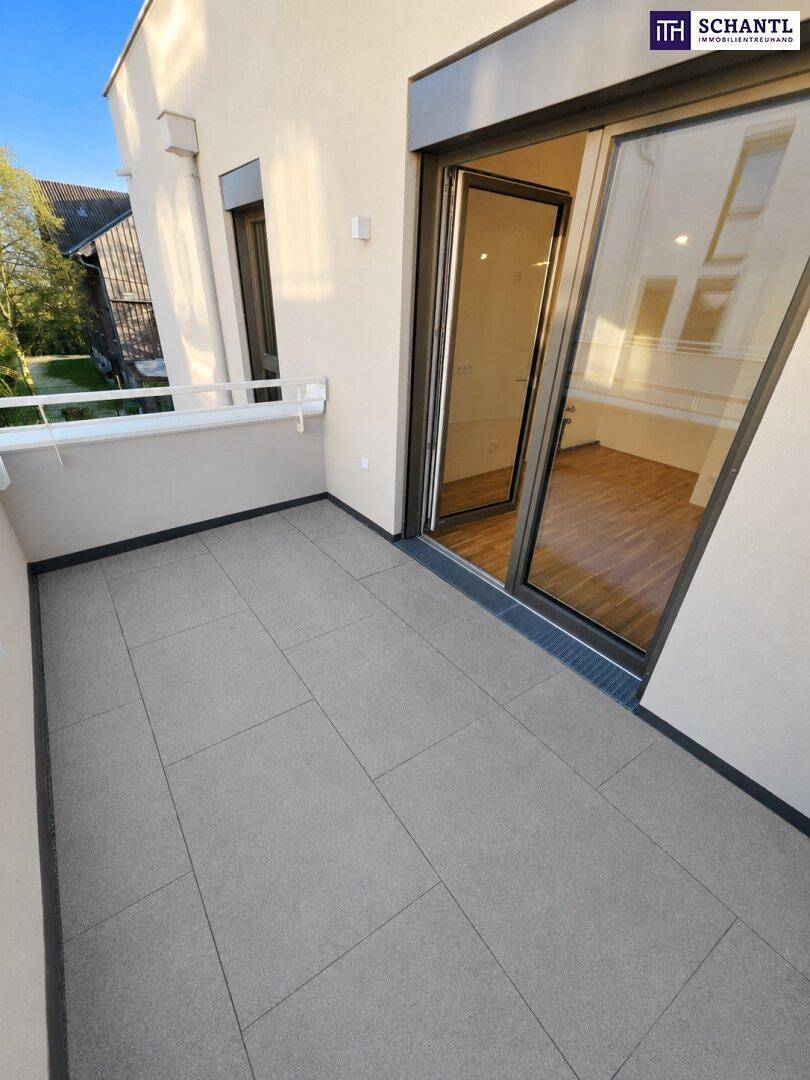 Heller Balkon mit grauen Fliesen und Zugang zu einem leeren Raum mit Holzfußboden.