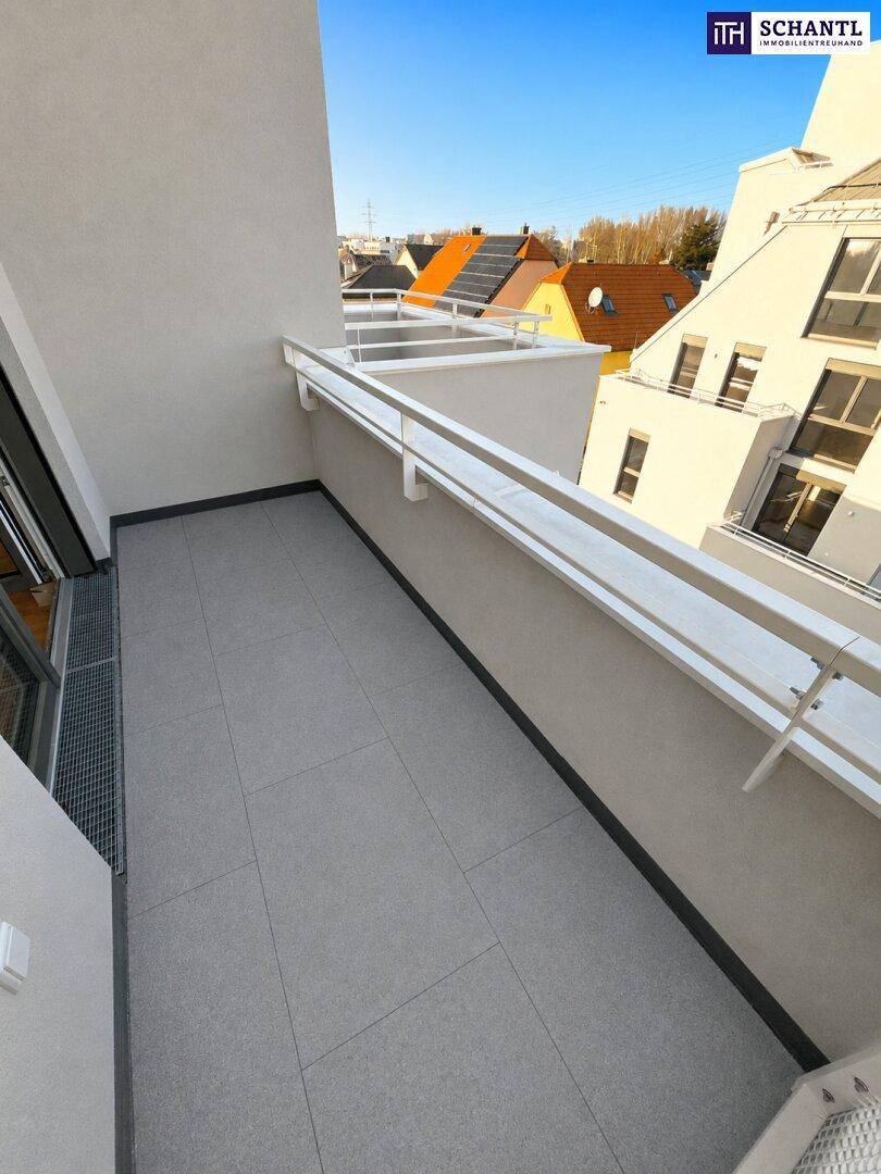 Heller Balkon mit grauen Fliesen und weißem Geländer, umgeben von Wohngebäuden.