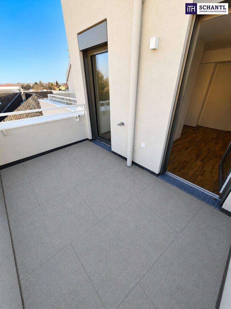 Kleiner Balkon mit grauen Fliesen und Zugang zu einem Innenraum mit Holzboden.
