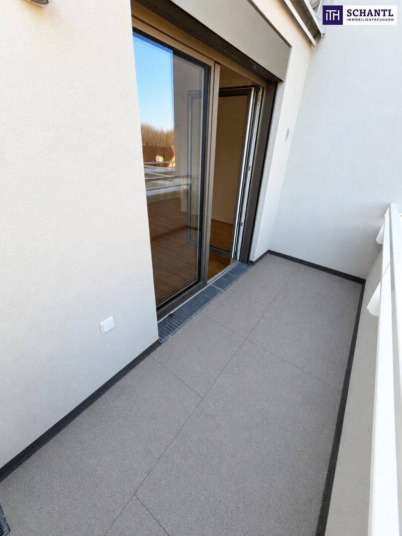 Balkon mit grauen Fliesen und großer Glastür, die viel Tageslicht hereinlässt.