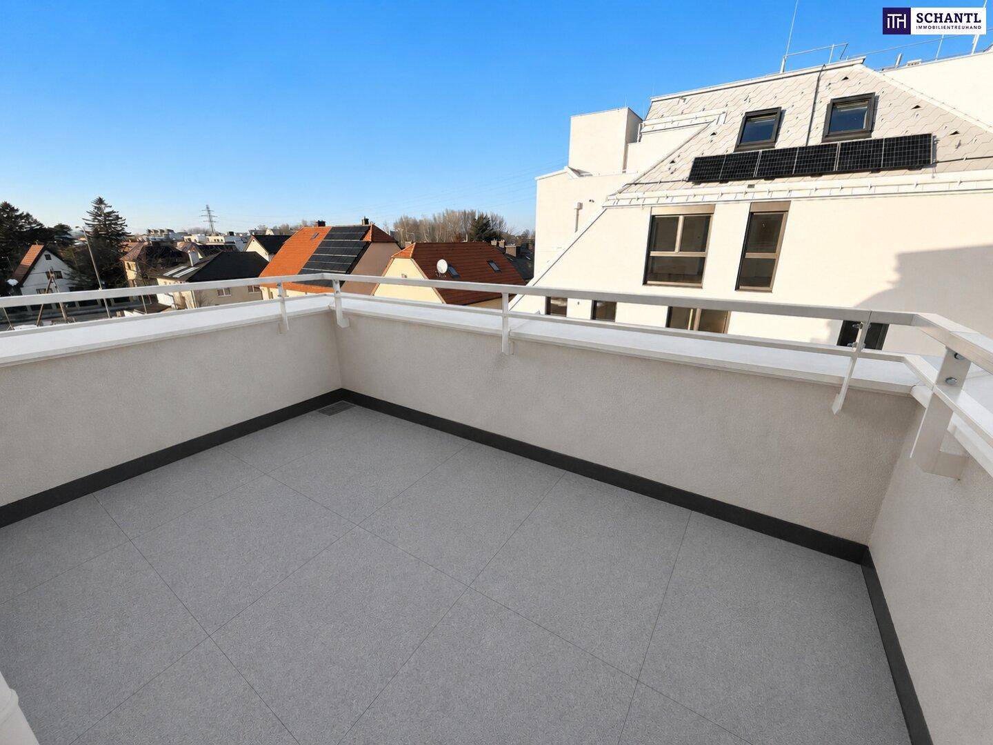 Sonniger Balkon mit grauen Bodenfliesen und Blick auf die umliegenden Dächer.