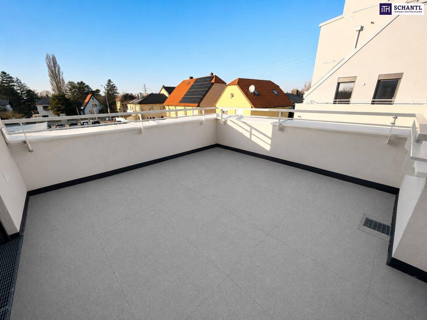 Weitläufige, geflieste Terrasse mit klarem Himmel und Blick auf die umliegenden Dächer der Nachbarschaft.