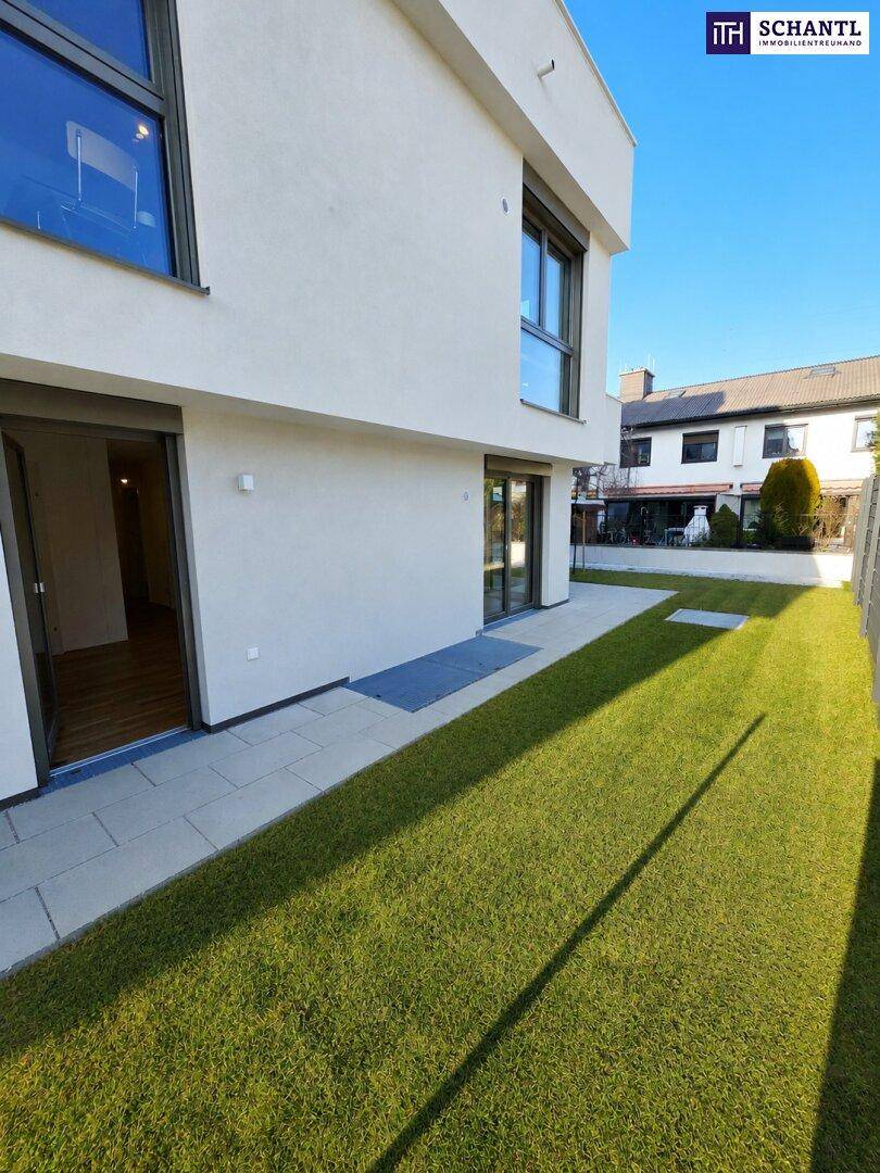 Gepflegter Gartenbereich mit Terrasse und direktem Zugang zu einem hellen Innenraum des Neubaus.