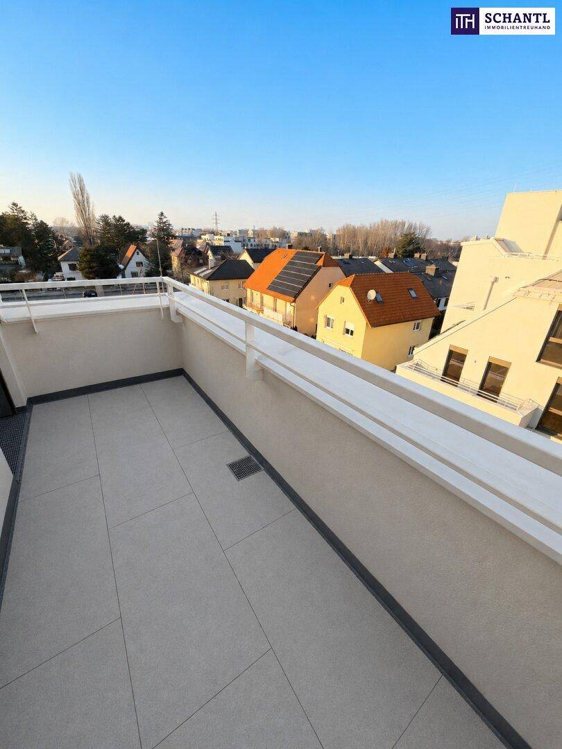 Heller Balkon mit Fliesenboden und Blick auf die Dächer der umliegenden Häuser bei Sonnenlicht.
