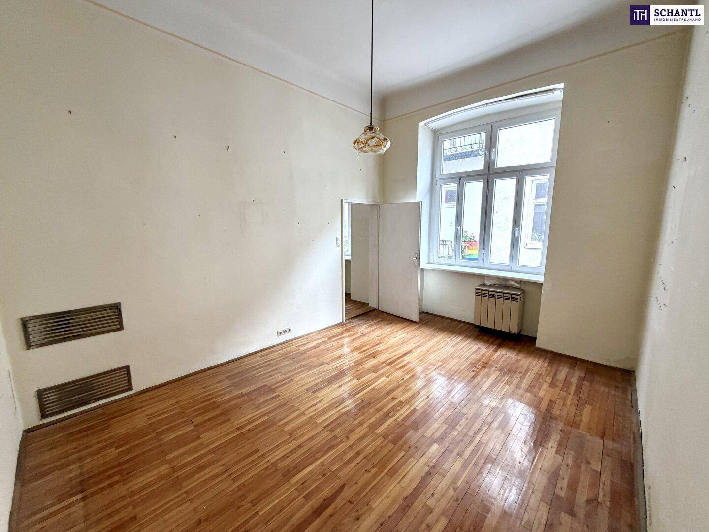 Geräumiges Zimmer mit Holzboden und zwei Lüftungsschlitzen, wartet auf eine umfassende Renovierung.