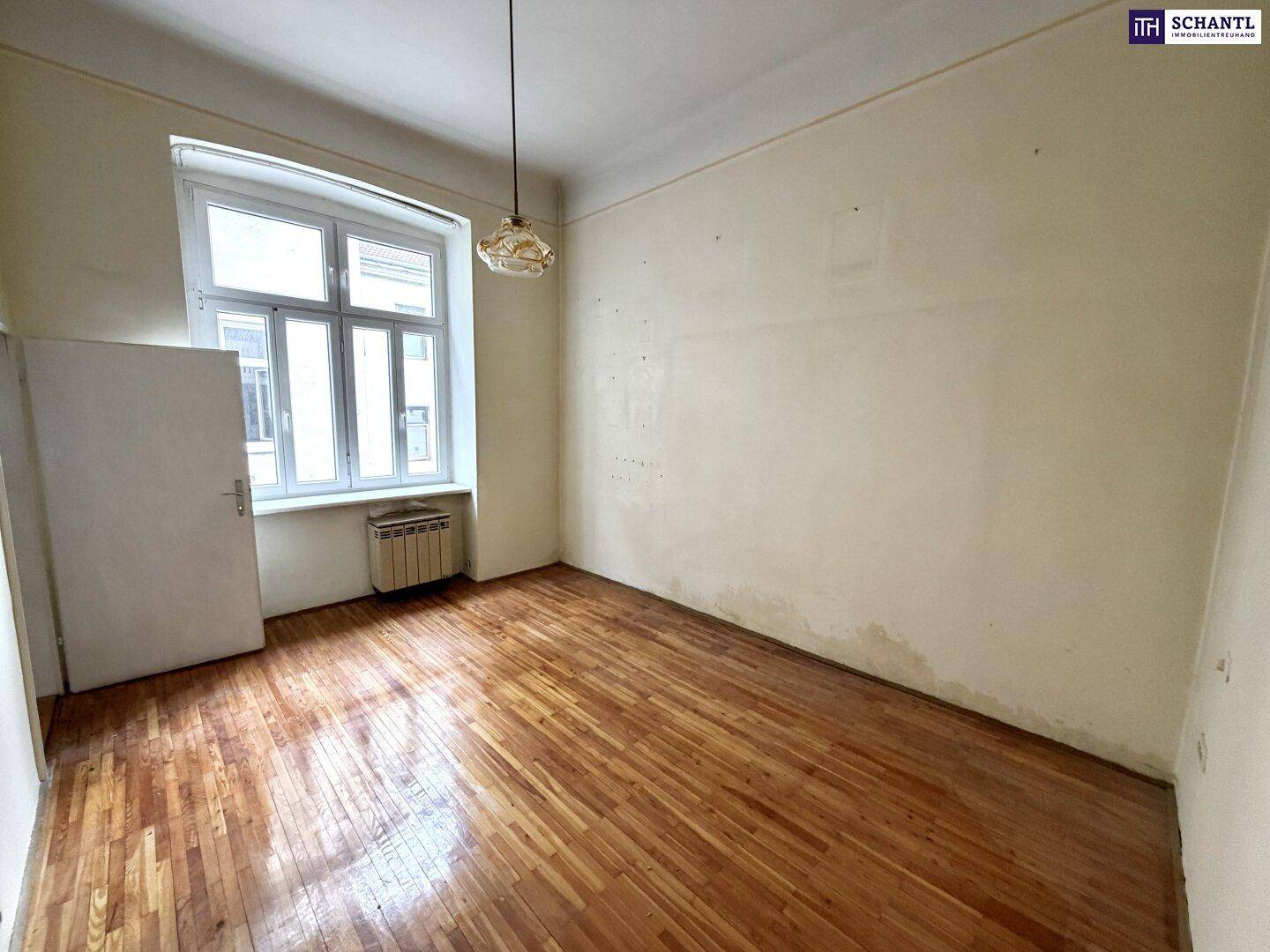 Unrenoviertes Zimmer mit Holzboden und Heizkörper unter dem Fenster, bietet Renovierungspotenzial.