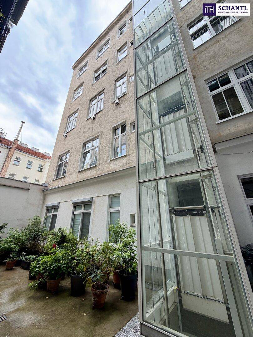 Begrünter Innenhof mit Pflanzen und einem modernen Glasaufzug, der die Stockwerke barrierefrei verbindet.