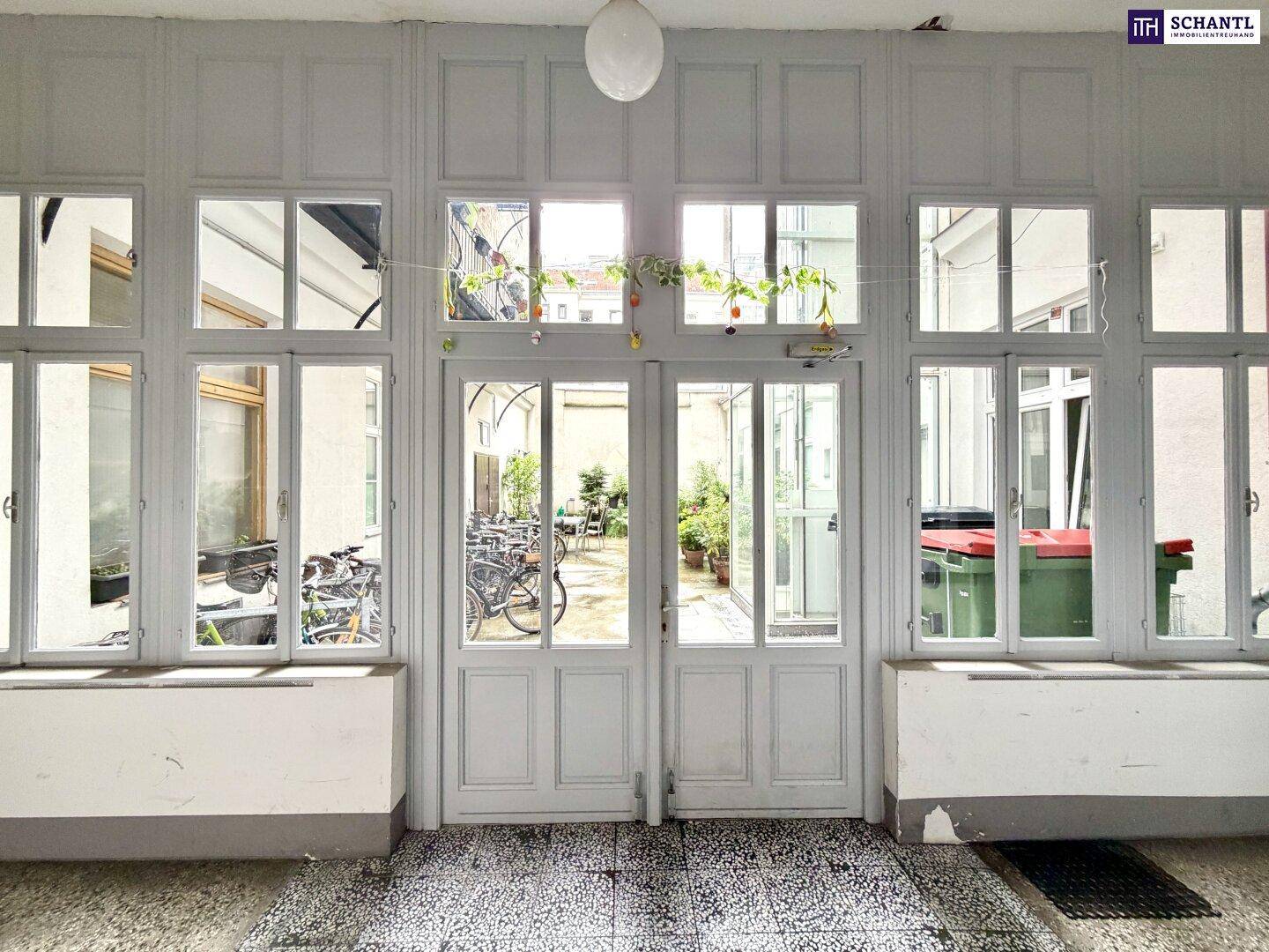 Heller Durchgangsbereich mit großen Fenstern, der zu einem begrünten Innenhof führt.
