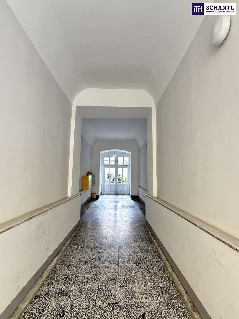 Langer Flur mit Terrazzoboden und hohen Decken, führt zu einem hellen Ausgang im Gebäude.