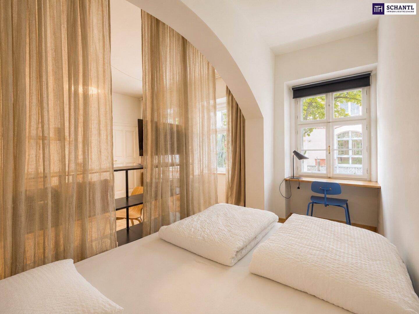 Schlafbereich mit Vorhängen zur Abtrennung, Schreibtisch am Fenster und Holzboden.