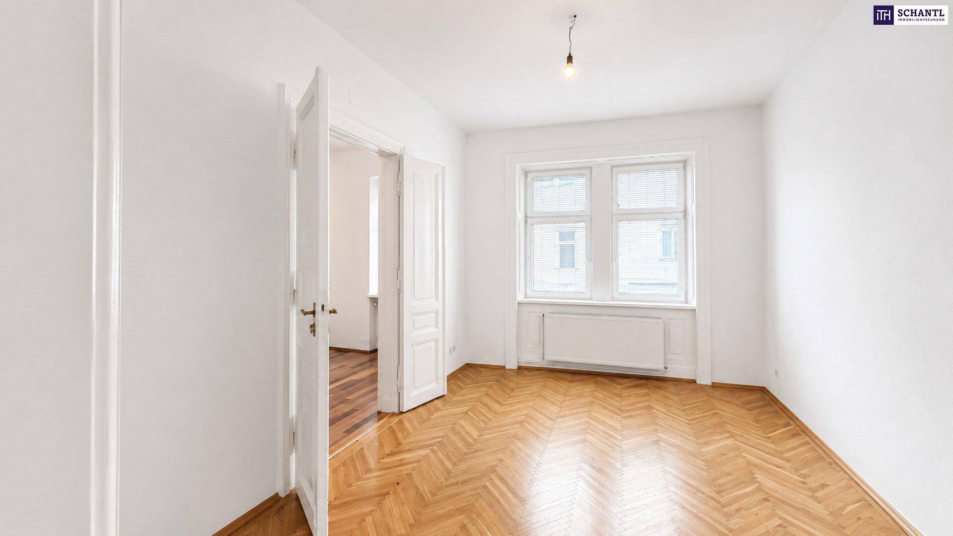 Geräumiges Zimmer mit klassischem Fischgrätparkett, hohen Decken und großen Fenstern.