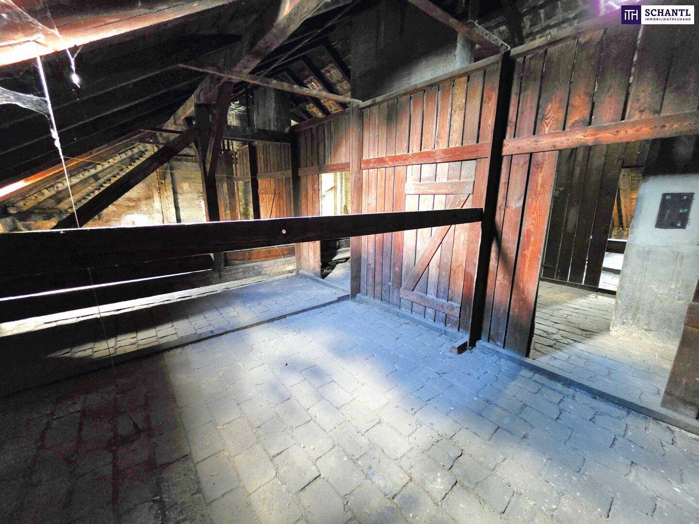Dachbodenbereich mit Holztrennwänden, sichtbaren Balken und einem Ziegelboden.
