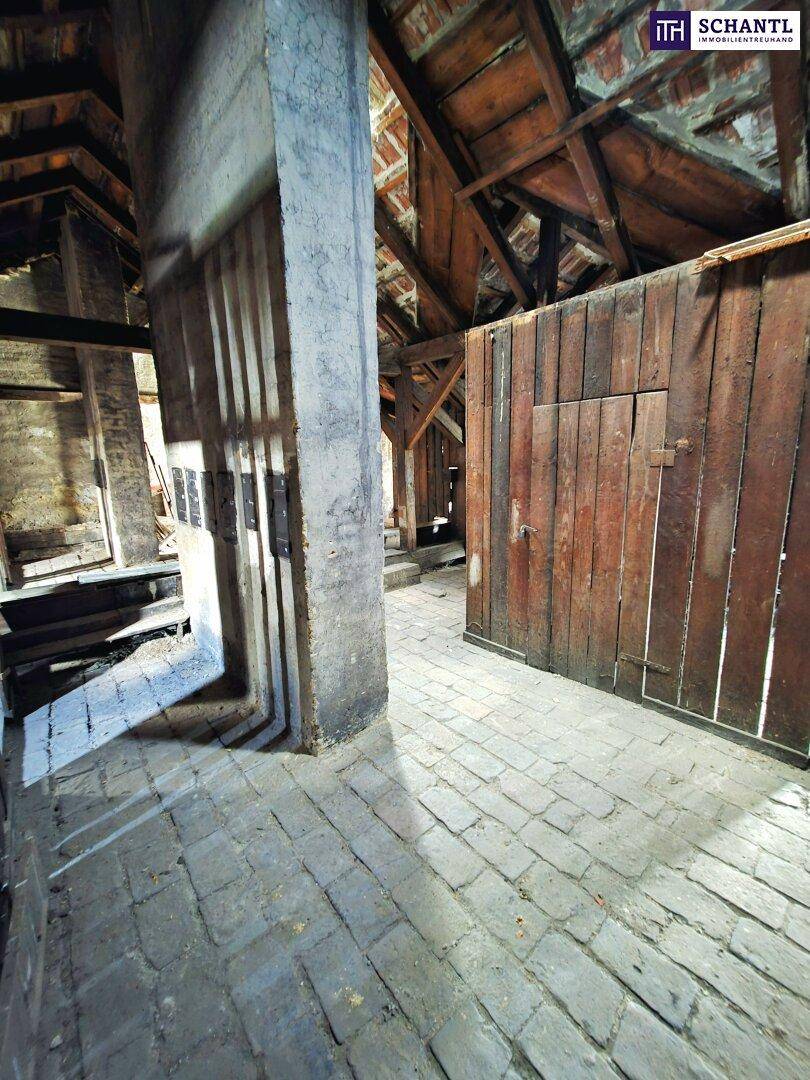 Blick in den Dachboden mit robusten Holzbalken, Ziegelboden und rustikalen Holzwänden.