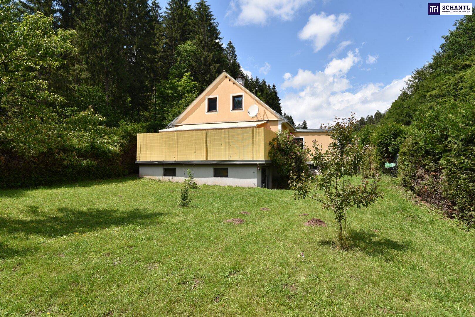 Seitenansicht des Hauses mit Balkon und großem Garten, umgeben von Wald und Natur.