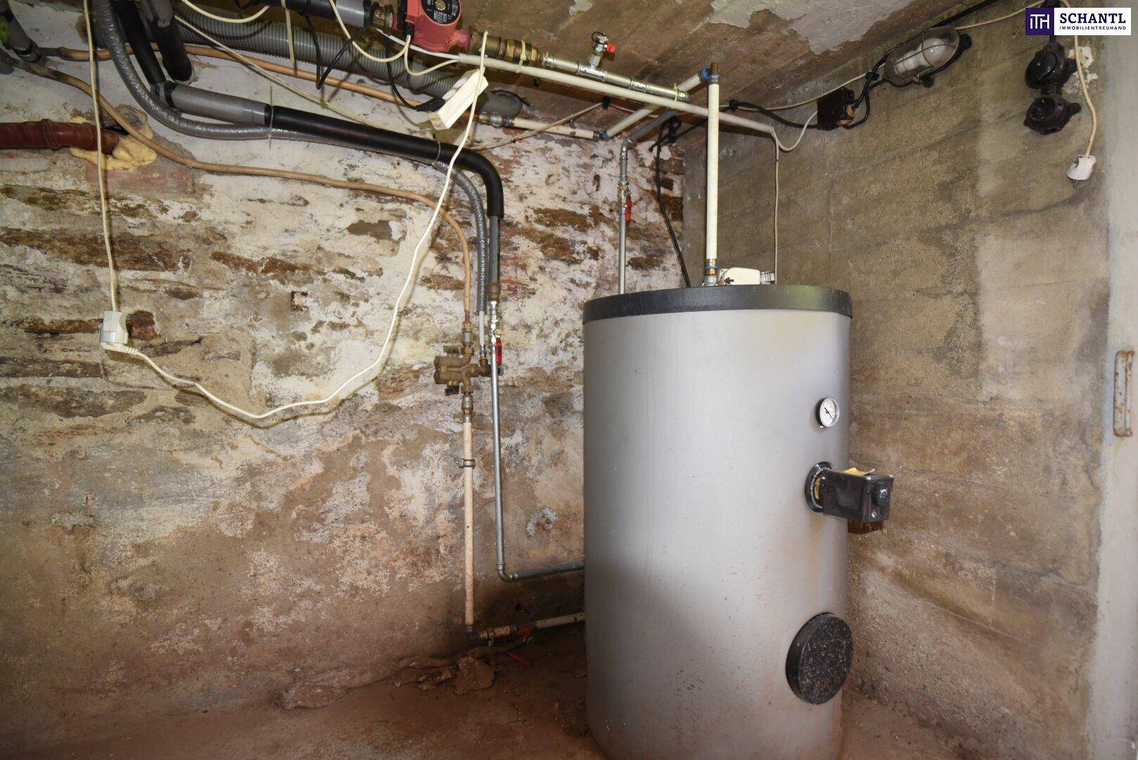 Kellerraum mit freiliegenden Rohren, rauen Wänden und einem Warmwasserbereiter.