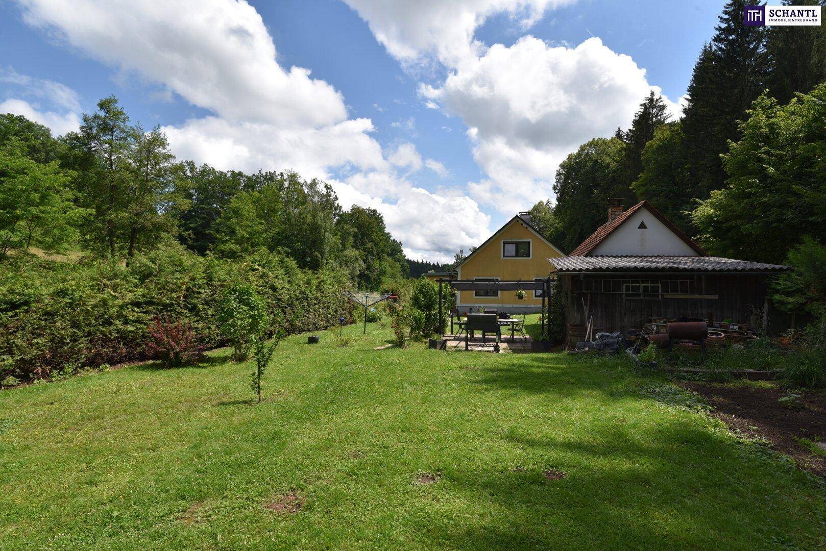 Blick auf die Rückseite des Hauses mit angrenzendem Schuppen und überdachtem Sitzbereich im Garten.
