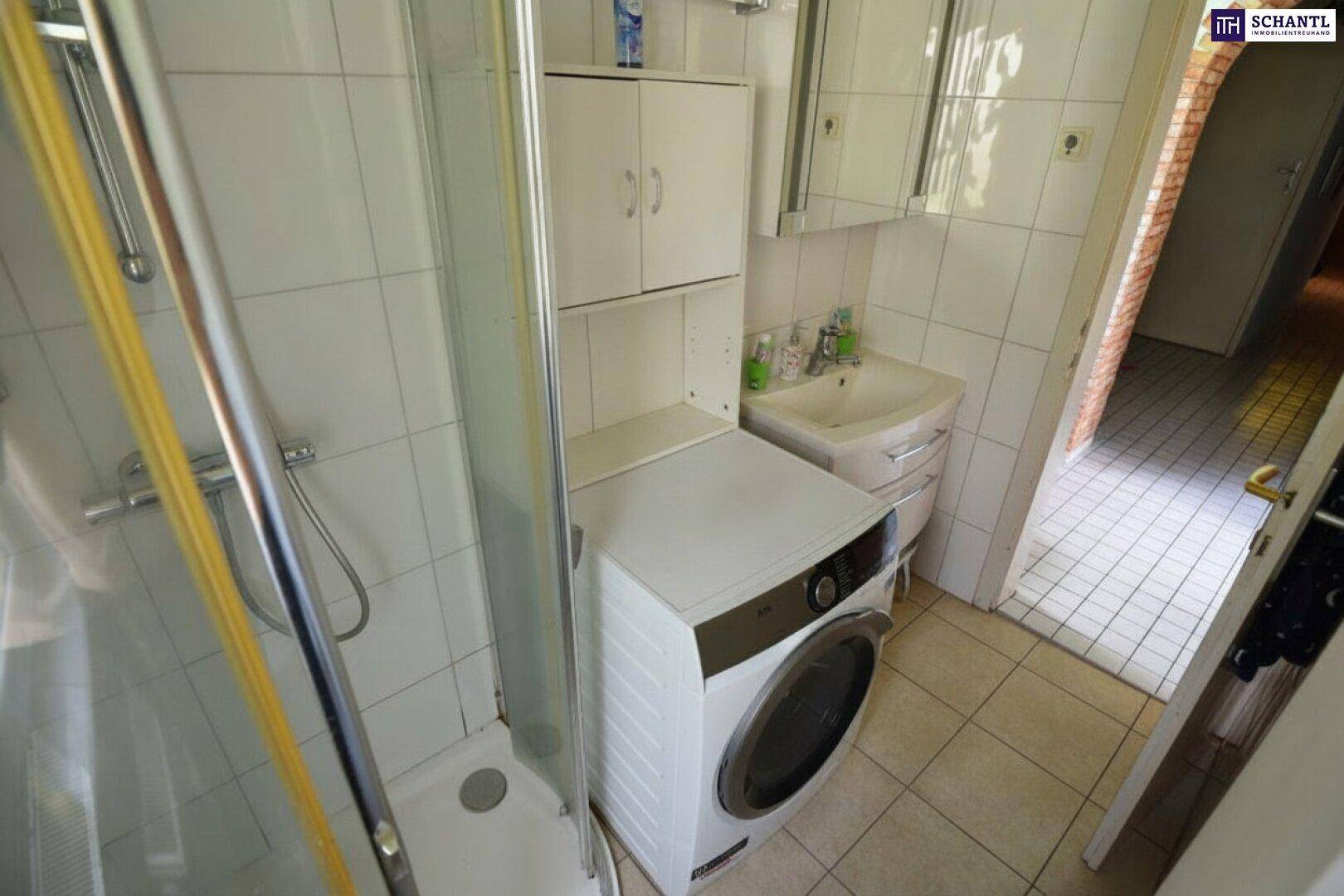Kleines Badezimmer mit Dusche, Waschbecken und Waschmaschine, komplett gefliest.