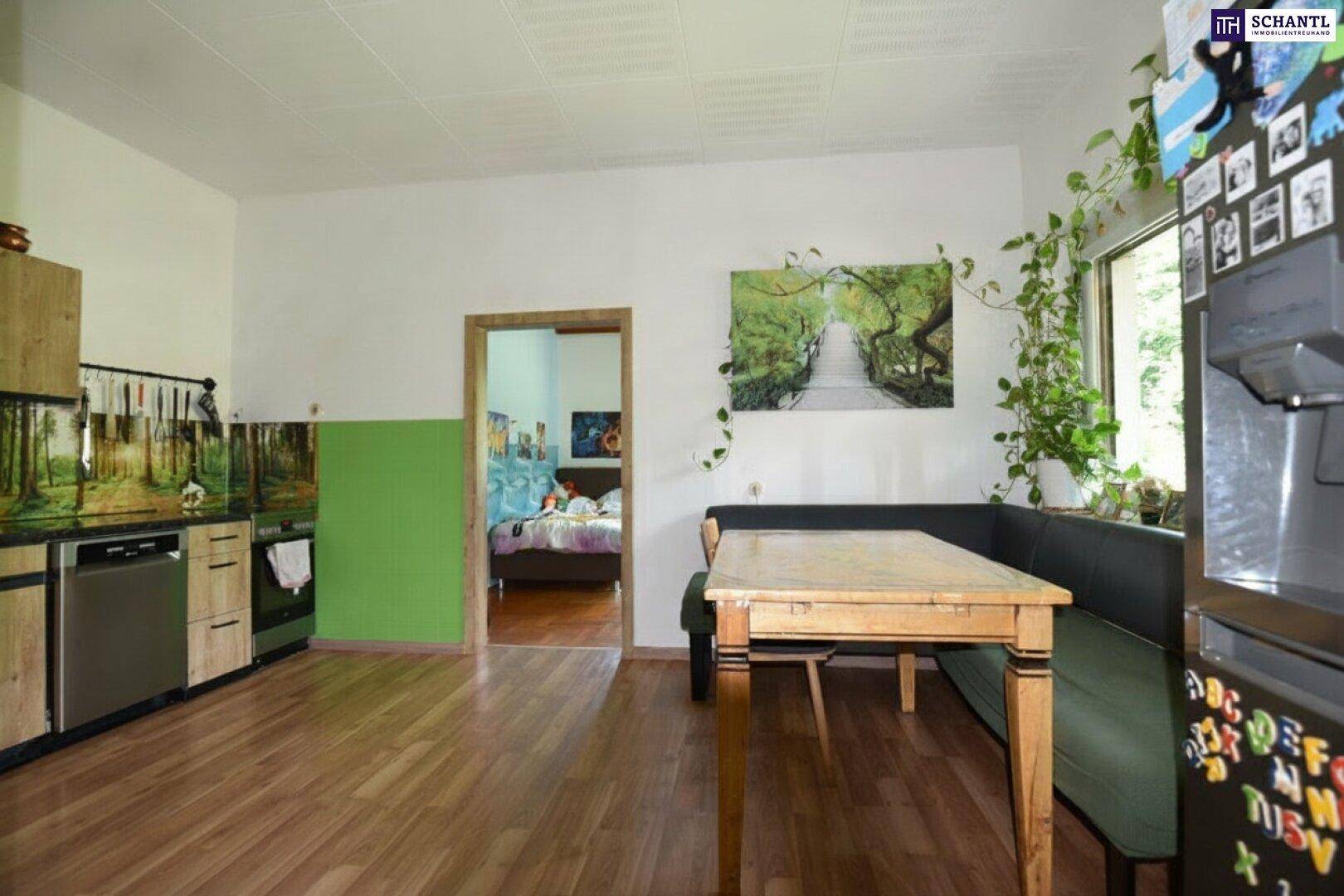 Wohnküche mit Holzboden, Essbereich und Blick in ein angrenzendes Schlafzimmer.