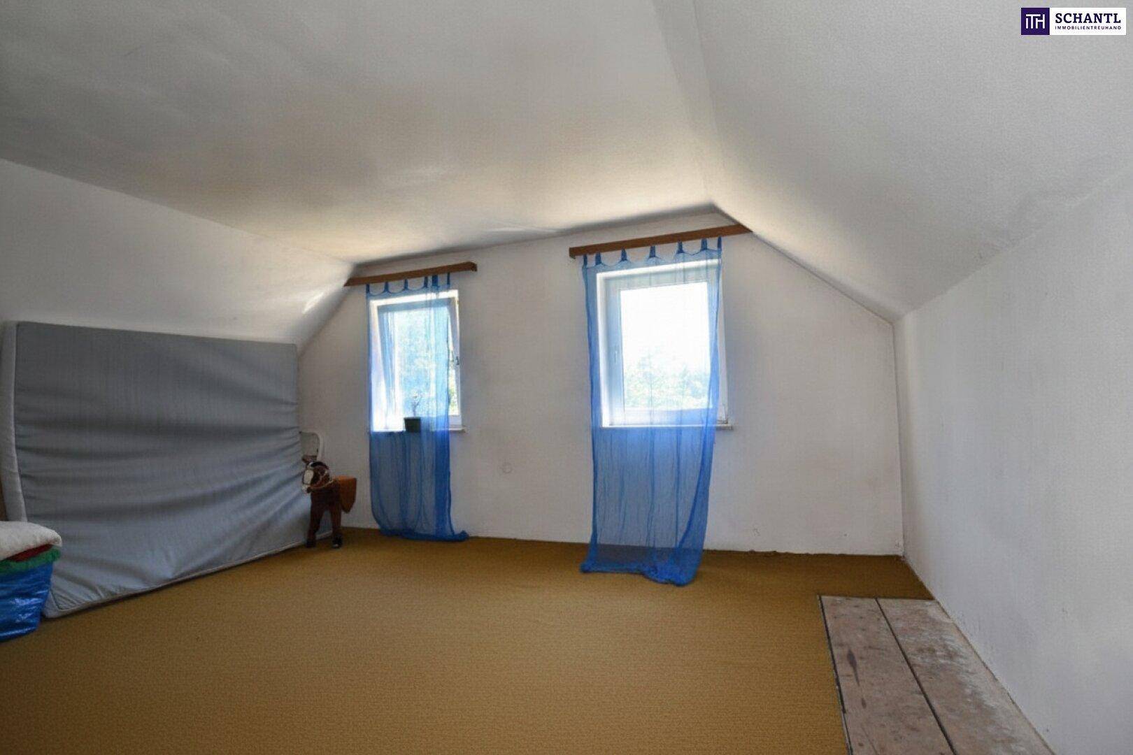 Dachzimmer mit schrägen Decken, zwei Fenstern mit blauen Vorhängen und Teppichboden.