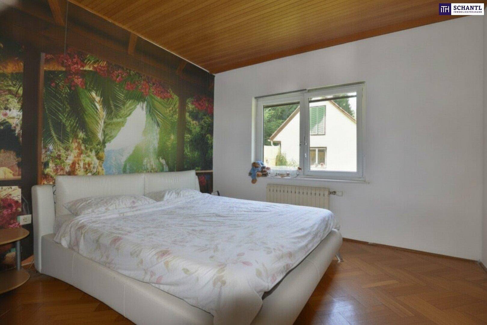 Schlafzimmer mit weißem Bett, Holzboden und einer auffälligen tropischen Tapete an der Wand.