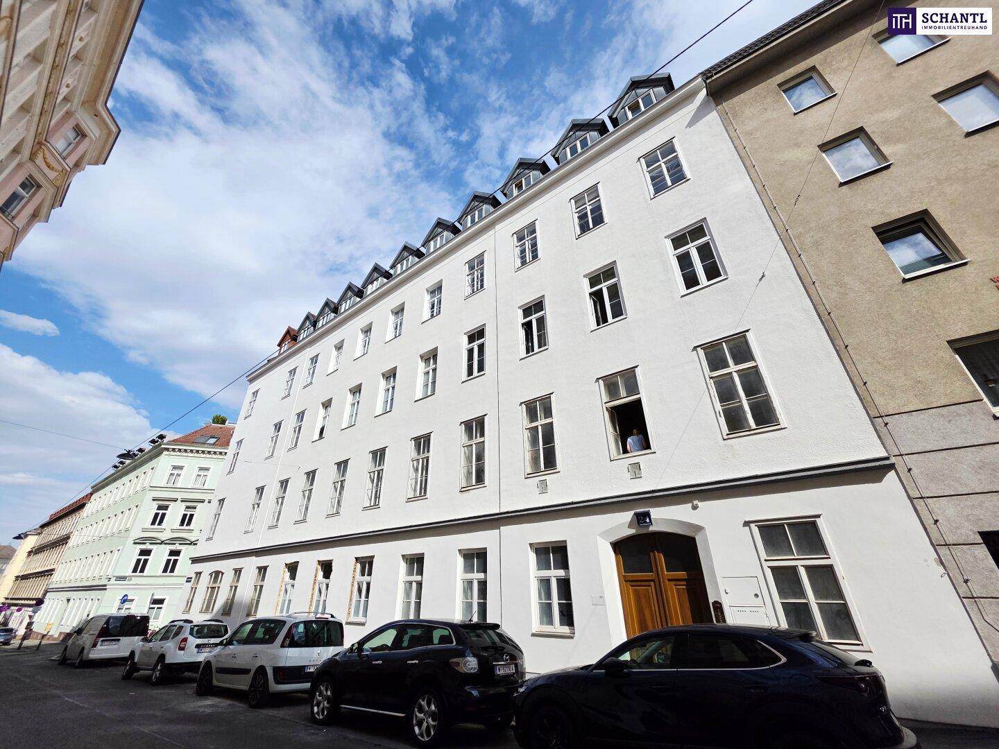 Historisches Mehrfamilienhaus mit weißer Fassade und vielen Fenstern in städtischer Umgebung.