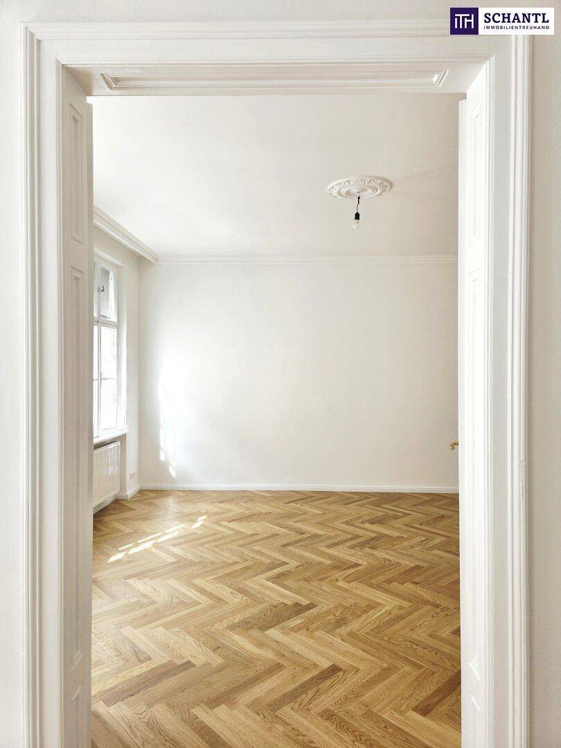 Blick durch eine Tür in ein helles Zimmer mit Fischgrätparkett und Stuckdecke.