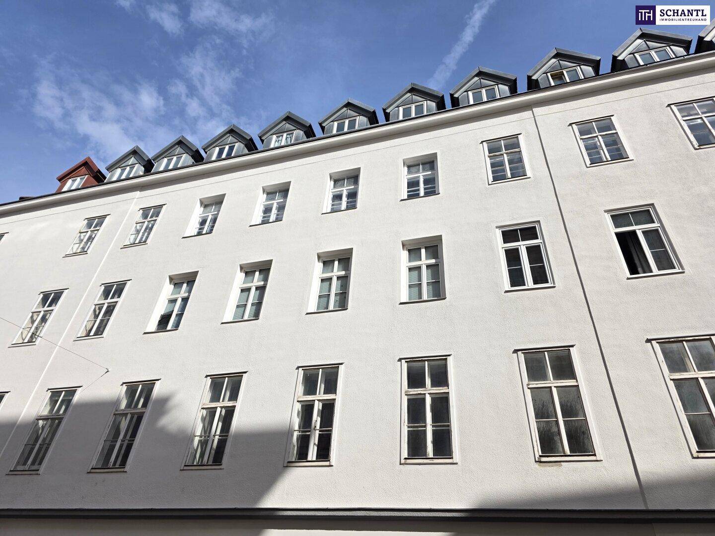 Detailansicht der weißen Fassade eines Altbaus mit zahlreichen Fenstern und Dachgauben.