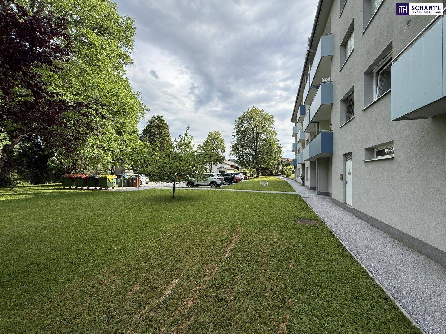 Seitenansicht des Wohngebäudes mit weitläufiger Rasenfläche und Parkplätzen im Hintergrund.