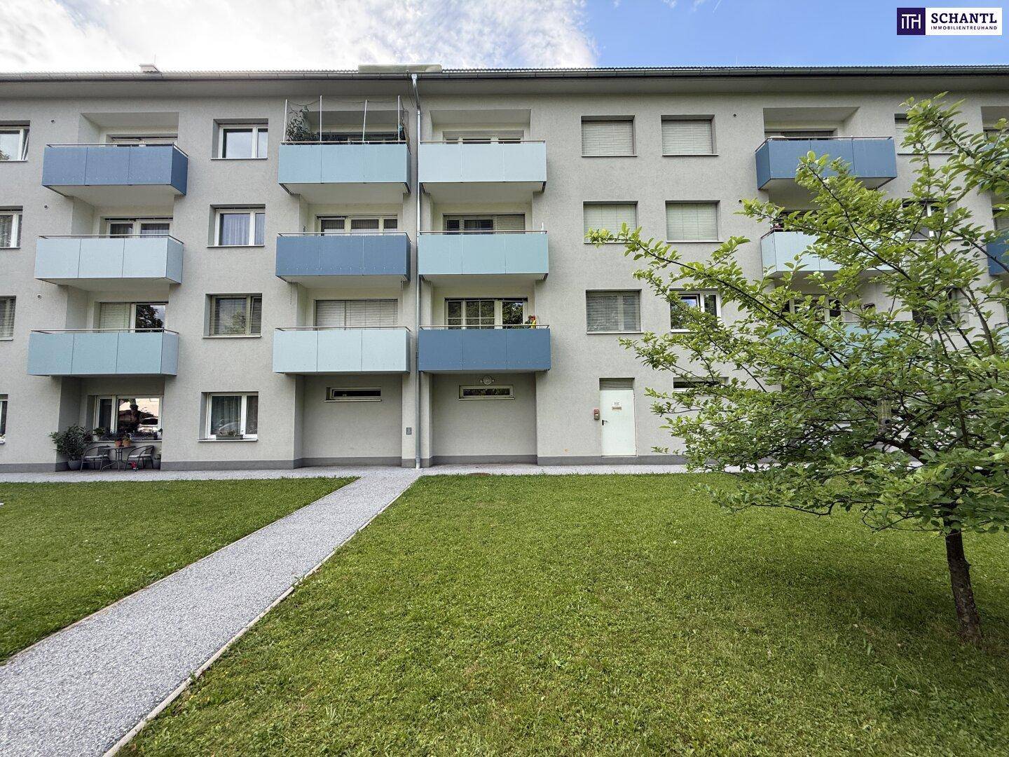 Ansicht des Mehrfamilienhauses mit farbigen Balkonen und einer gepflegten Rasenfläche.