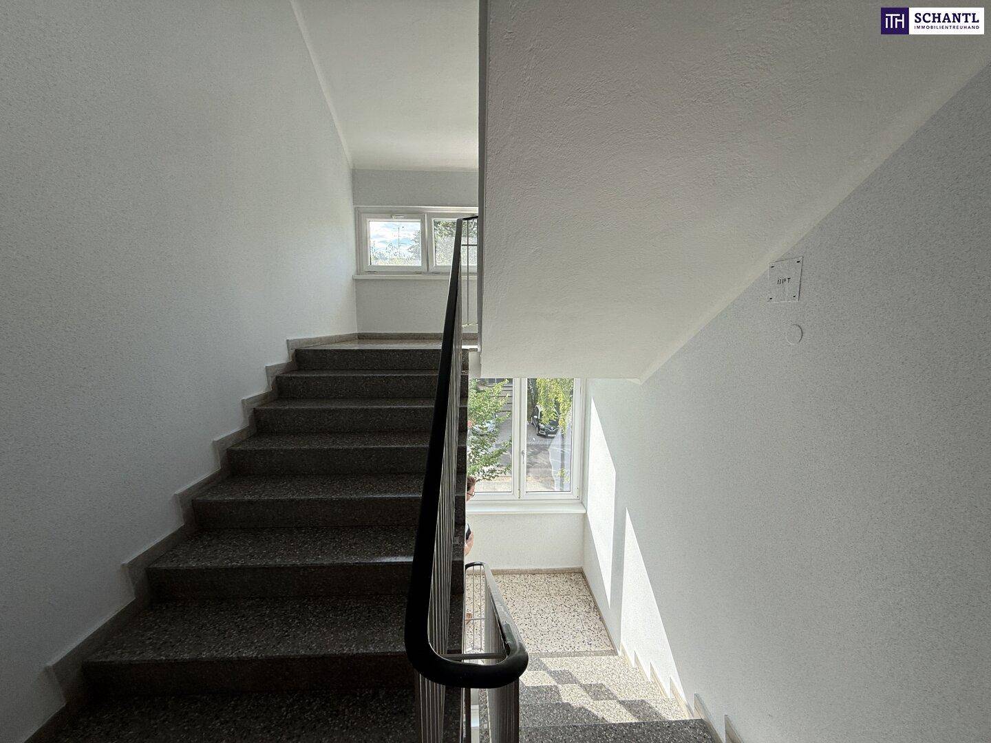 Treppenhaus mit Terrazzostufen und Metallgeländer, gut beleuchtet durch Tageslicht.