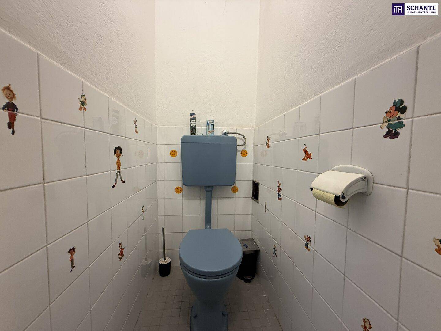 Separates WC mit blauer Toilette und verspielten Fliesenaufklebern an den Wänden.