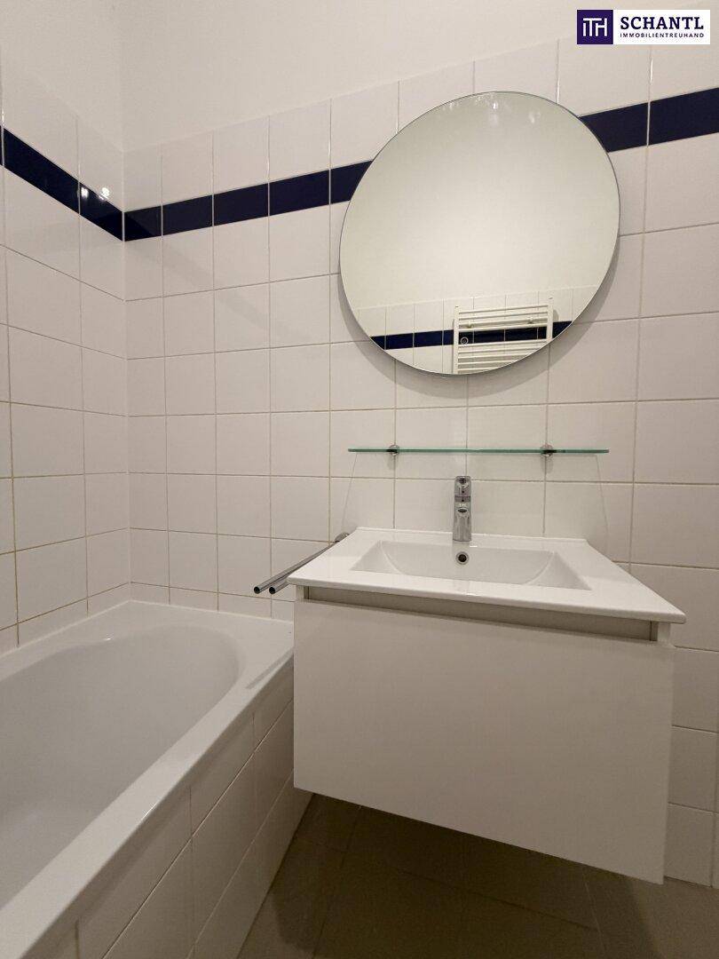 Modernes Badezimmer mit weißem Waschtisch, rundem Spiegel und Badewanne, inklusive Handtuchheizkörper.