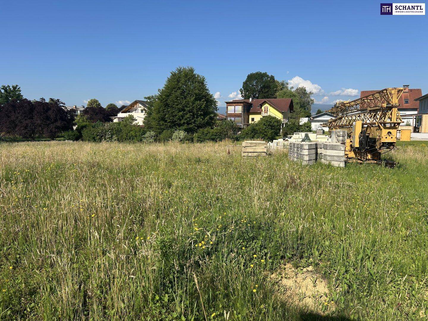 Grünfläche mit Baugeräten und Materialien, umgeben von Wohnhäusern unter klarem, blauem Himmel.