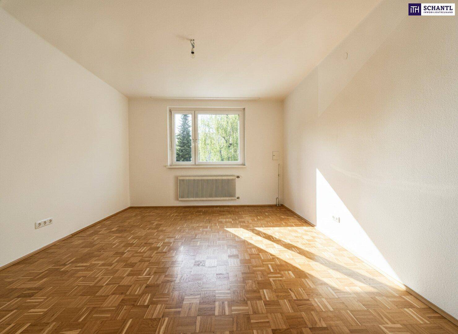 Lichtdurchflutetes Zimmer mit klassischem Parkettboden und einem großen Fenster, das viel Tageslicht hereinlässt.
