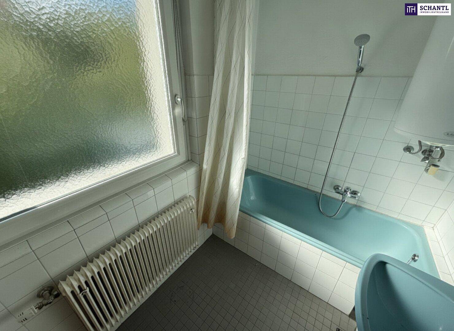 Badezimmer mit blauer Badewanne, weißen Wandfliesen und einem Fenster für natürliche Belüftung.
