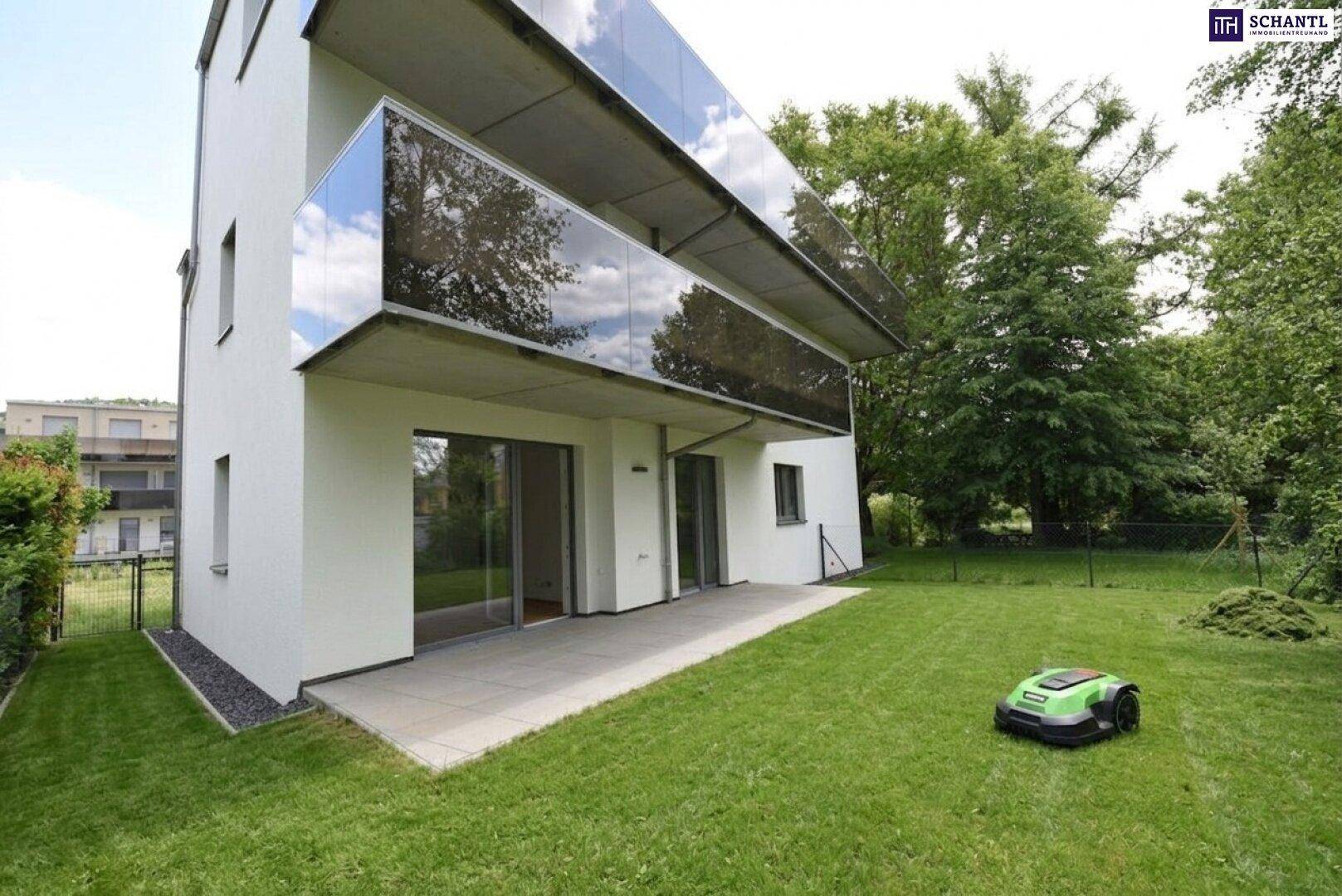 Ansicht des modernen Gebäudes mit Terrasse und einem großen, grünen Garten mit Mähroboter.
